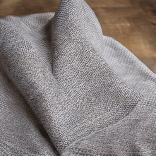 A close-up of a houndstooth-patterned crochet scarf in shades of black, white, and gray, with a subtle sheen, draped elegantly over a minimalist wooden or stone background, with a few loose yarn threads.